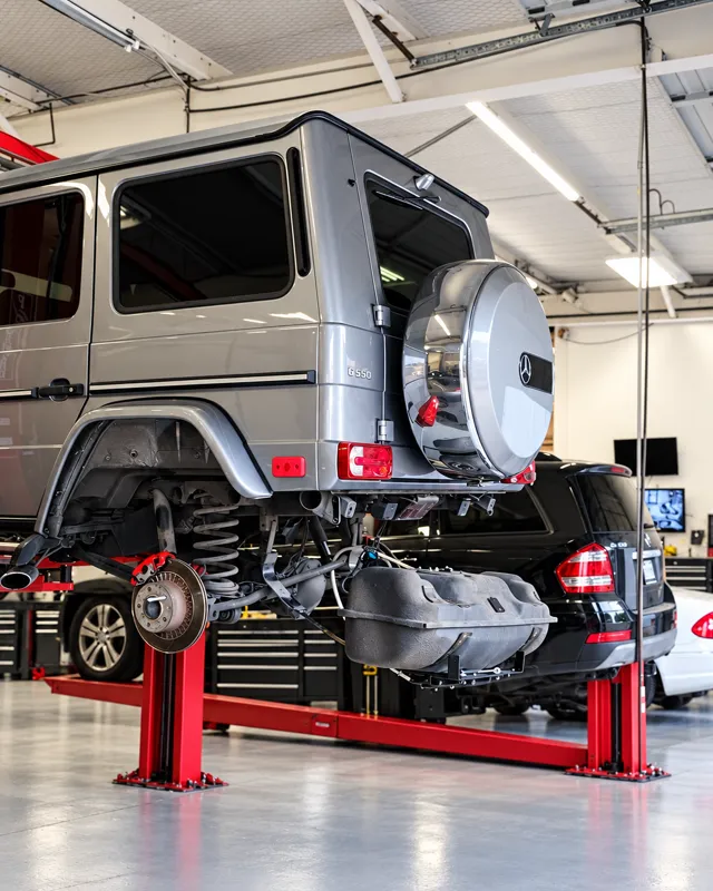 An SUV raised on a red two-post lift with its rear brake assembly exposed for service.
