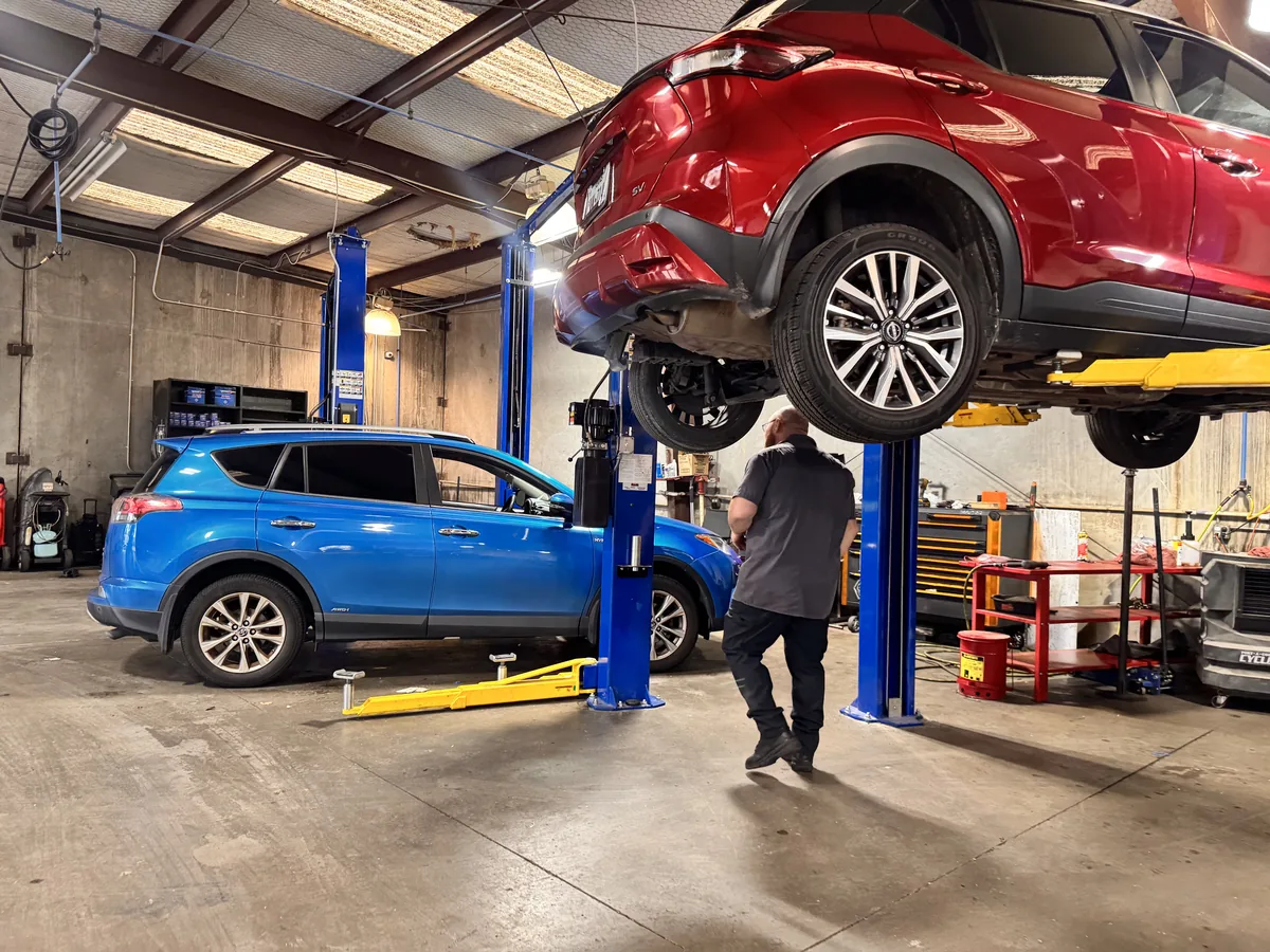 A wide view of an Integrity 1st service bay with vehicles on lifts and a technician at work