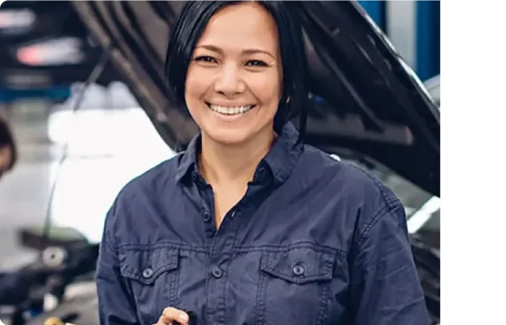 Smiling auto technician in a navy work shirt standing in front of a car with its hood open