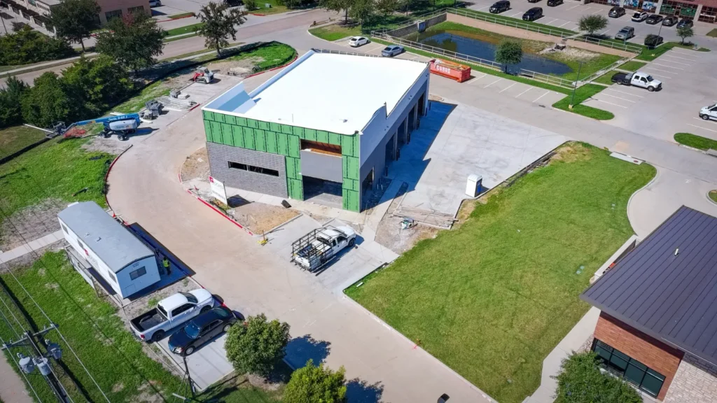 Aerial view of the new Integrity 1st Car Pros shop under construction in Anna, Texas, with the roof finished and stone going up the front elevation