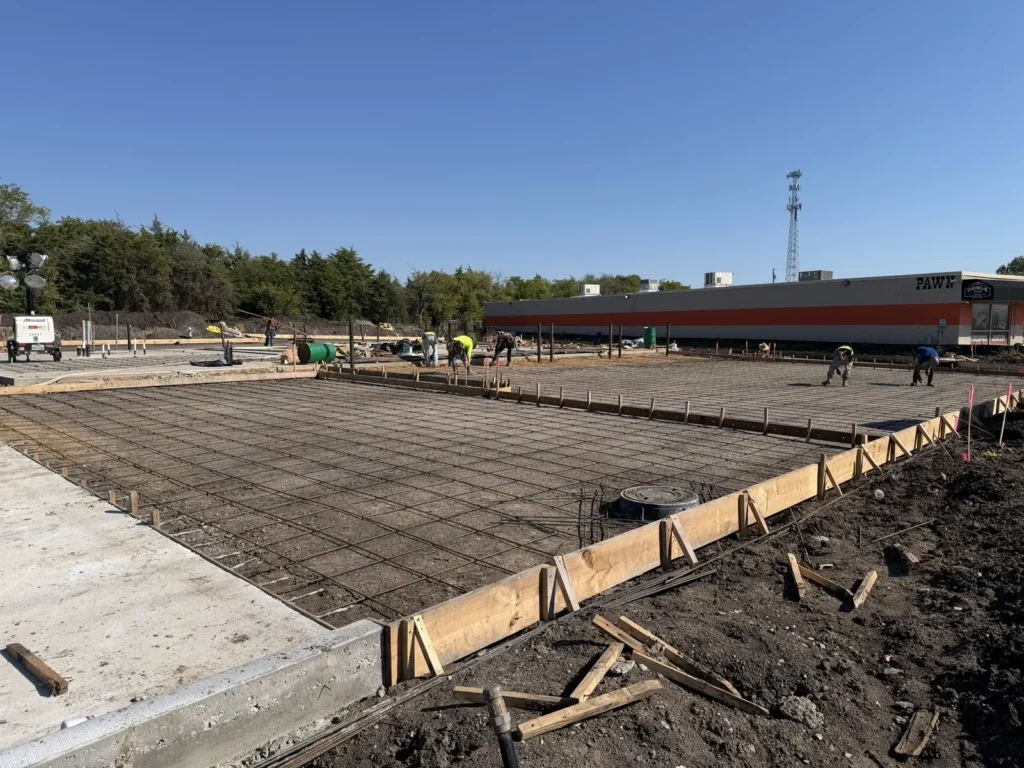 Steel reinforcing mat laid across the formed slab at the new Wylie site in October 2026, with the neighbouring retail building behind